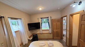A hotel room with a bed, a TV mounted on the wall, a window with curtains, and a wooden door.
