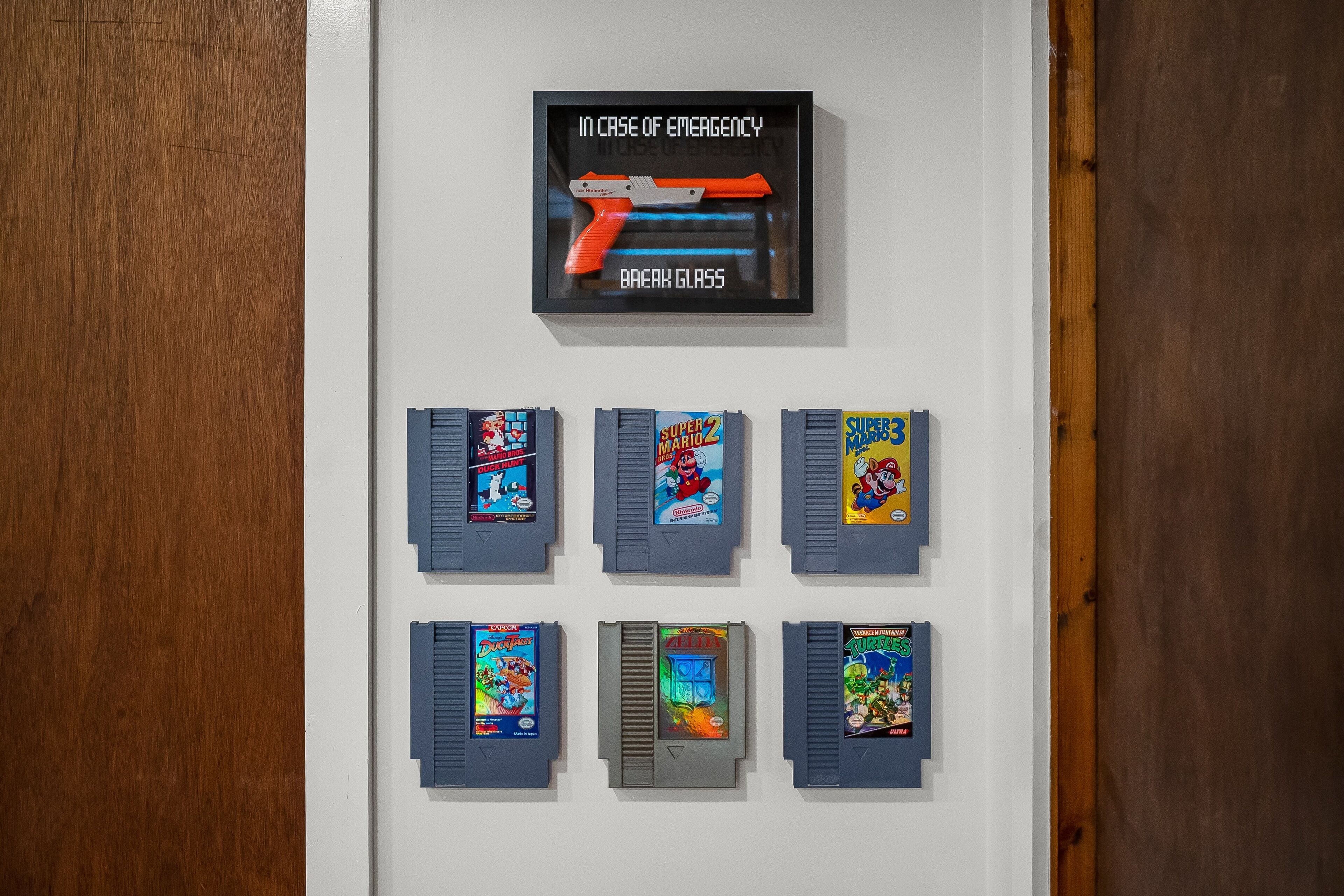 A wall with a framed emergency instruction sign and eight retro video game cartridges.