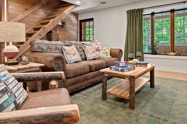 A cozy living room with a brown leather sofa, wooden coffee table, and a green patterned rug. - The Lodge At Tunkhannock Creek (Tunkhannock)