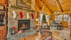 Interior acogedor de una cabaña con chimenea de piedra, calcetines navideños, un árbol decorado y muebles de madera rústica.