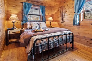 A cozy wooden cabin bedroom with a bed, two bedside tables, lamps, and a tennis racket on the wall.