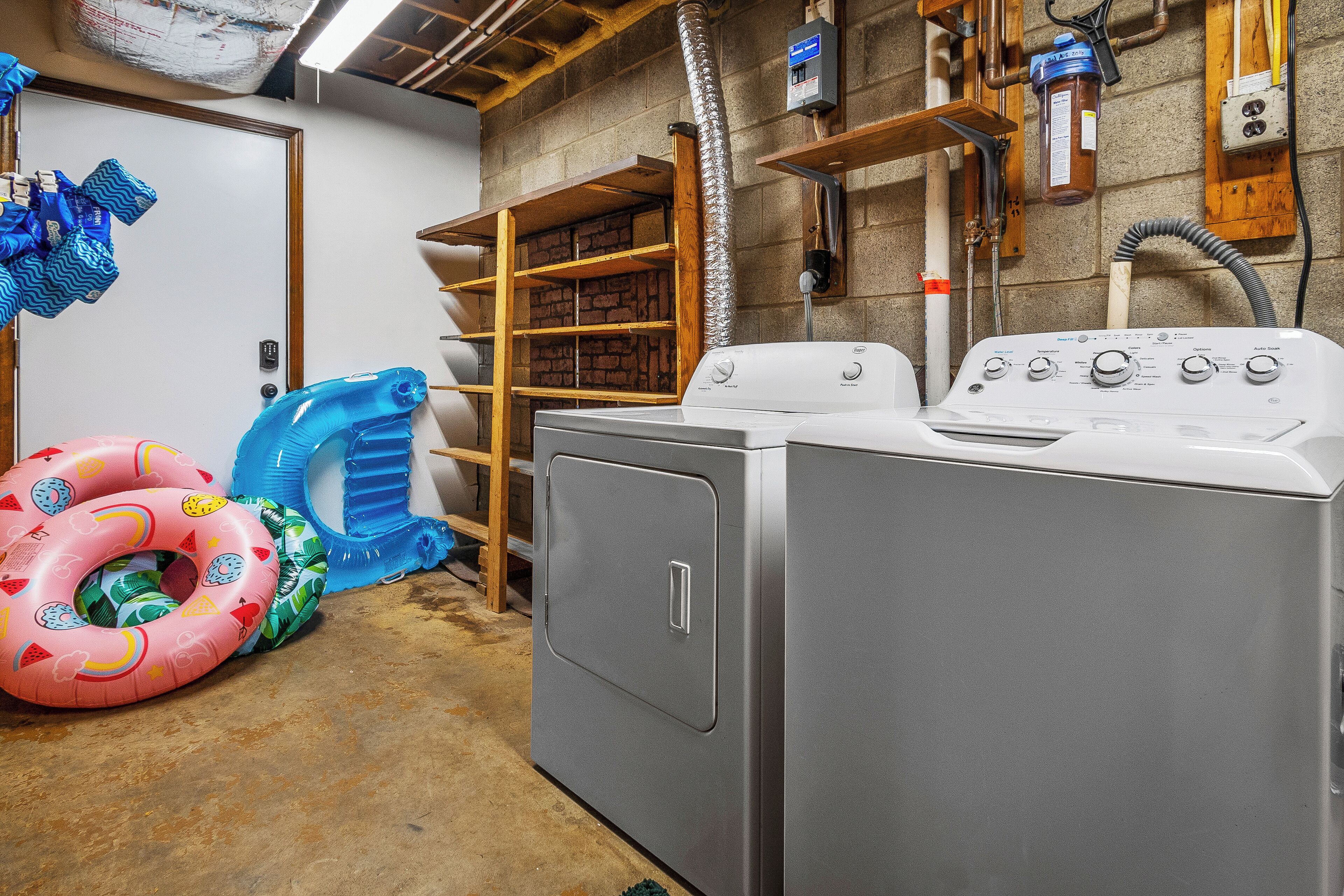A laundry room with stacked washer and dryer, a brick wall, and a wooden shelf unit.