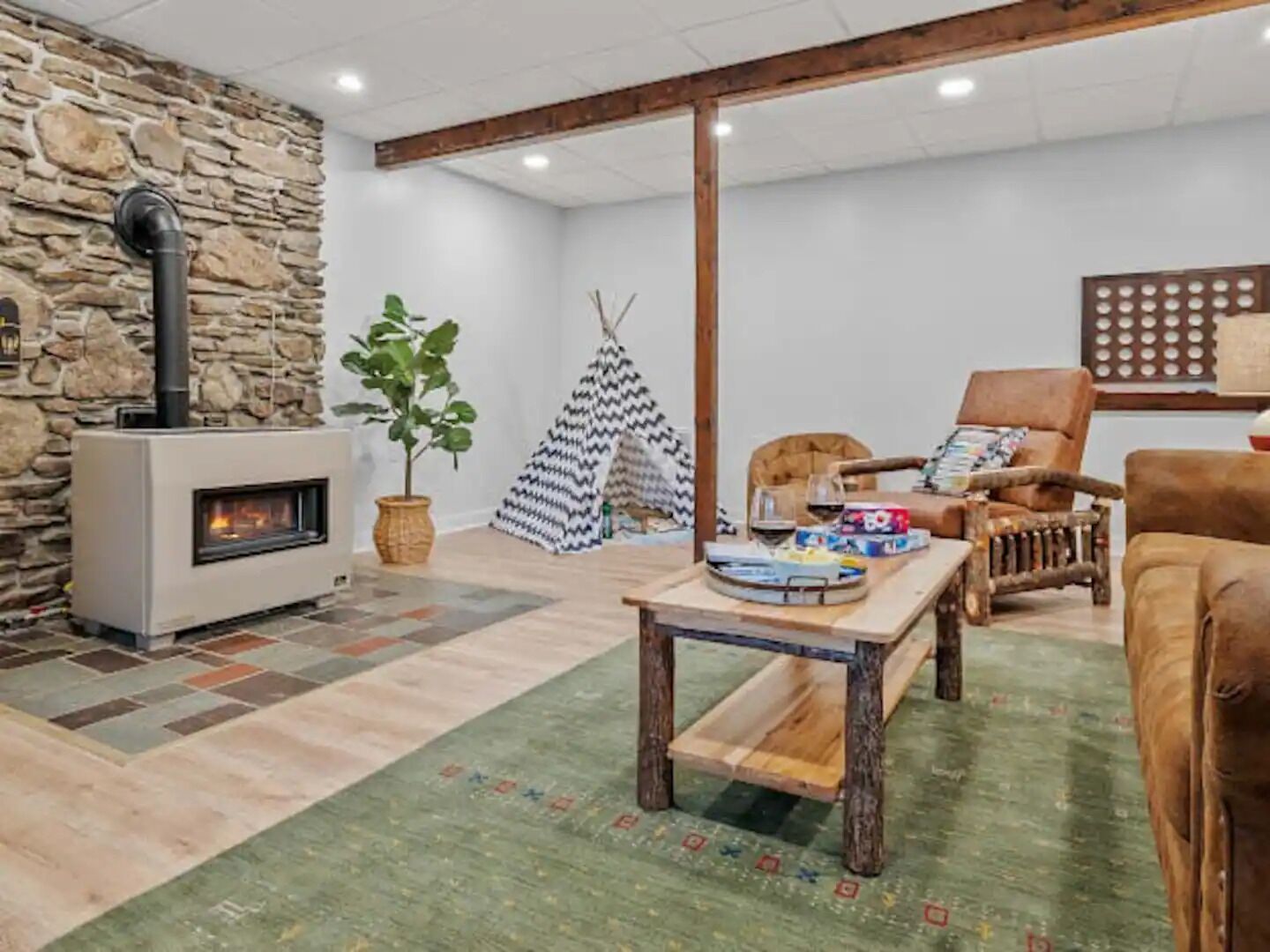 A cozy living room with a stone wall, a fireplace, a wooden table, and a comfortable seating area.