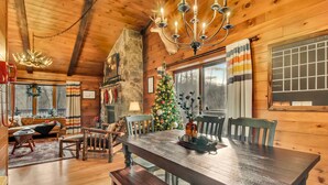 Un interior acogedor de cabaña con una mesa de comedor de madera, sillas, chimenea, un árbol de Navidad y una pared de piedra.