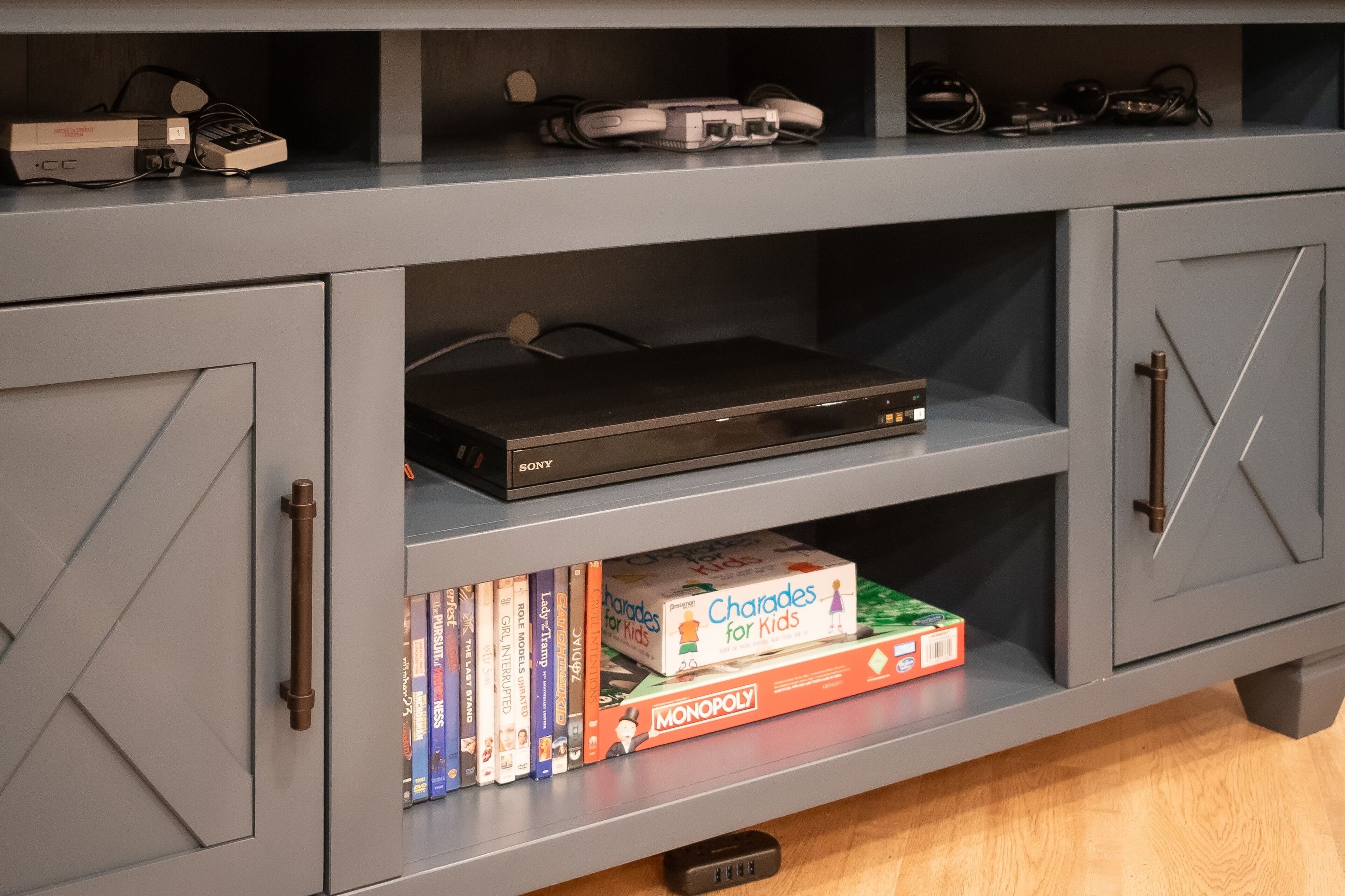 A grey entertainment unit with a DVD player, gaming consoles, and board games.