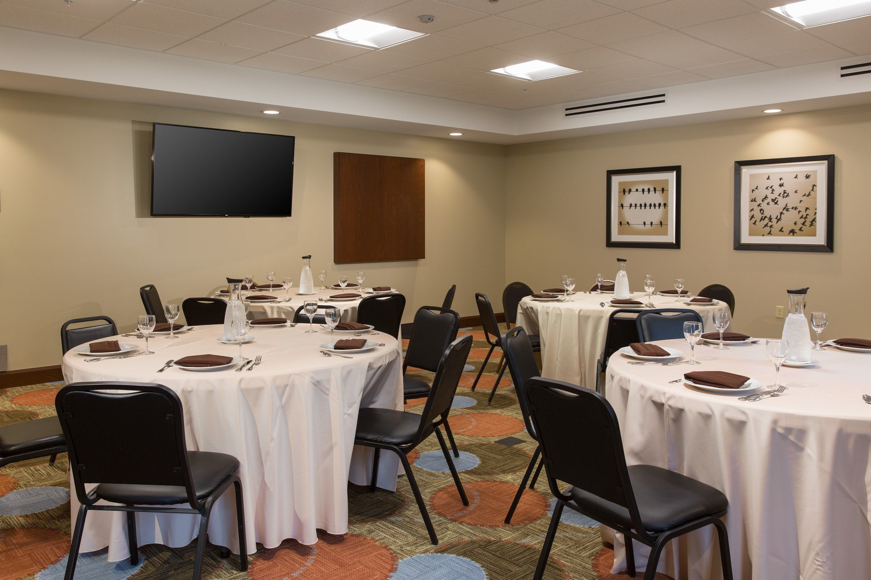 A conference room with round tables, black chairs, and white tablecloths.