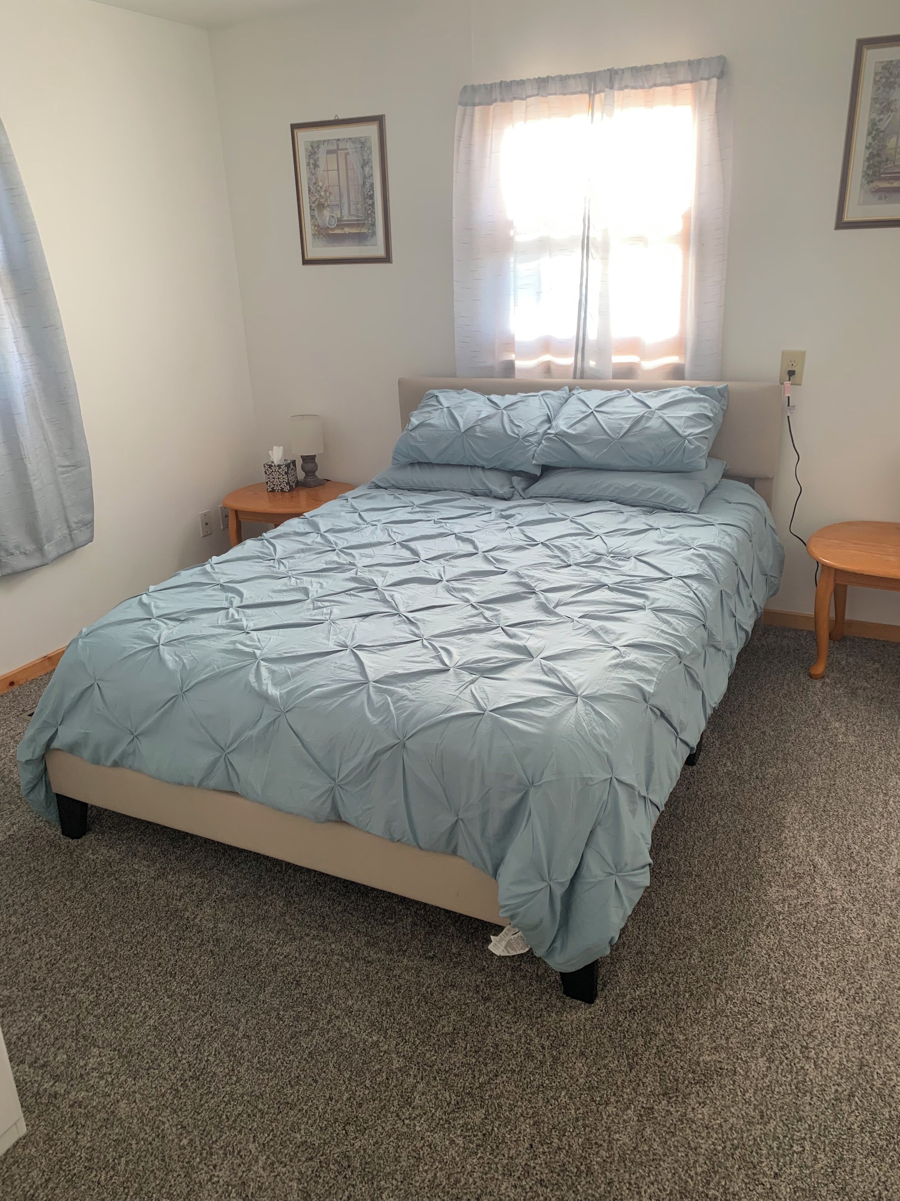 A bedroom with a bed, a nightstand, a lamp, and a window with curtains.