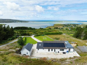 A house with a solar panel roof, a well-maintained lawn, and a view of a lake and distant landscape.