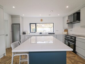 A modern kitchen with a central island, white cabinetry, a stainless steel refrigerator, and a built-in oven.