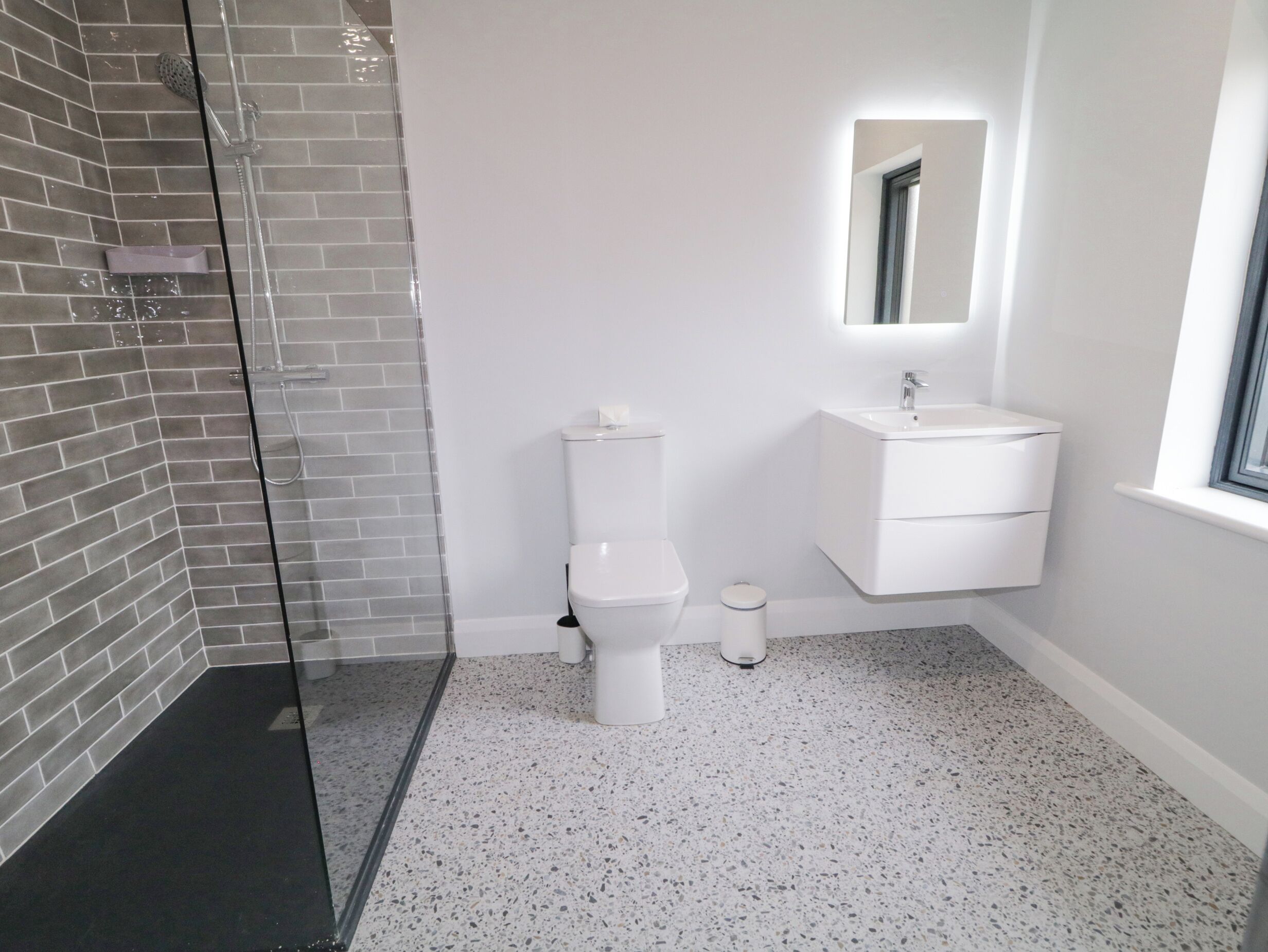 A modern bathroom with a glass shower enclosure, a white toilet, and a sink with a mirror above it.