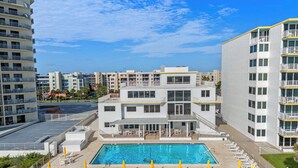 A modern hotel with a rooftop pool, multiple balconies, and a view of other buildings.