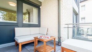 A balcony with a wooden table, a cushioned bench, and a small sofa.