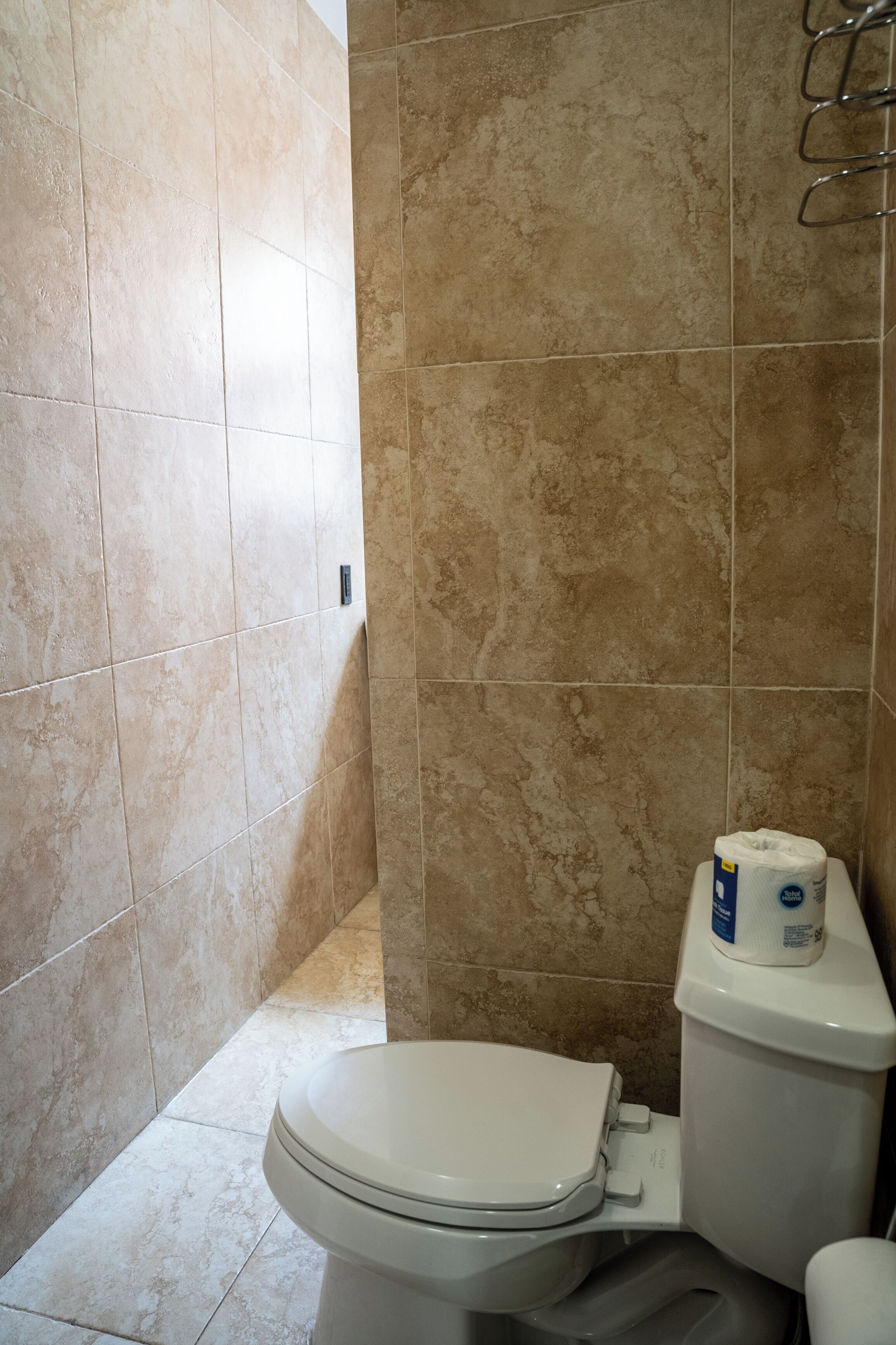 Un baño con baldosas color beige, un inodoro blanco y un dispensador de toallas de papel.
