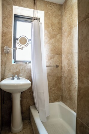 A bathroom with a pedestal sink, a bathtub, and a window with a shower curtain.