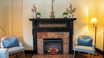 A living room with a fireplace, two patterned armchairs, a floor lamp, and decorative items on the mantel.