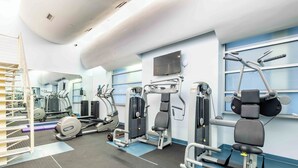 A modern gym with various exercise equipment, a large mirror, and a window with blinds.