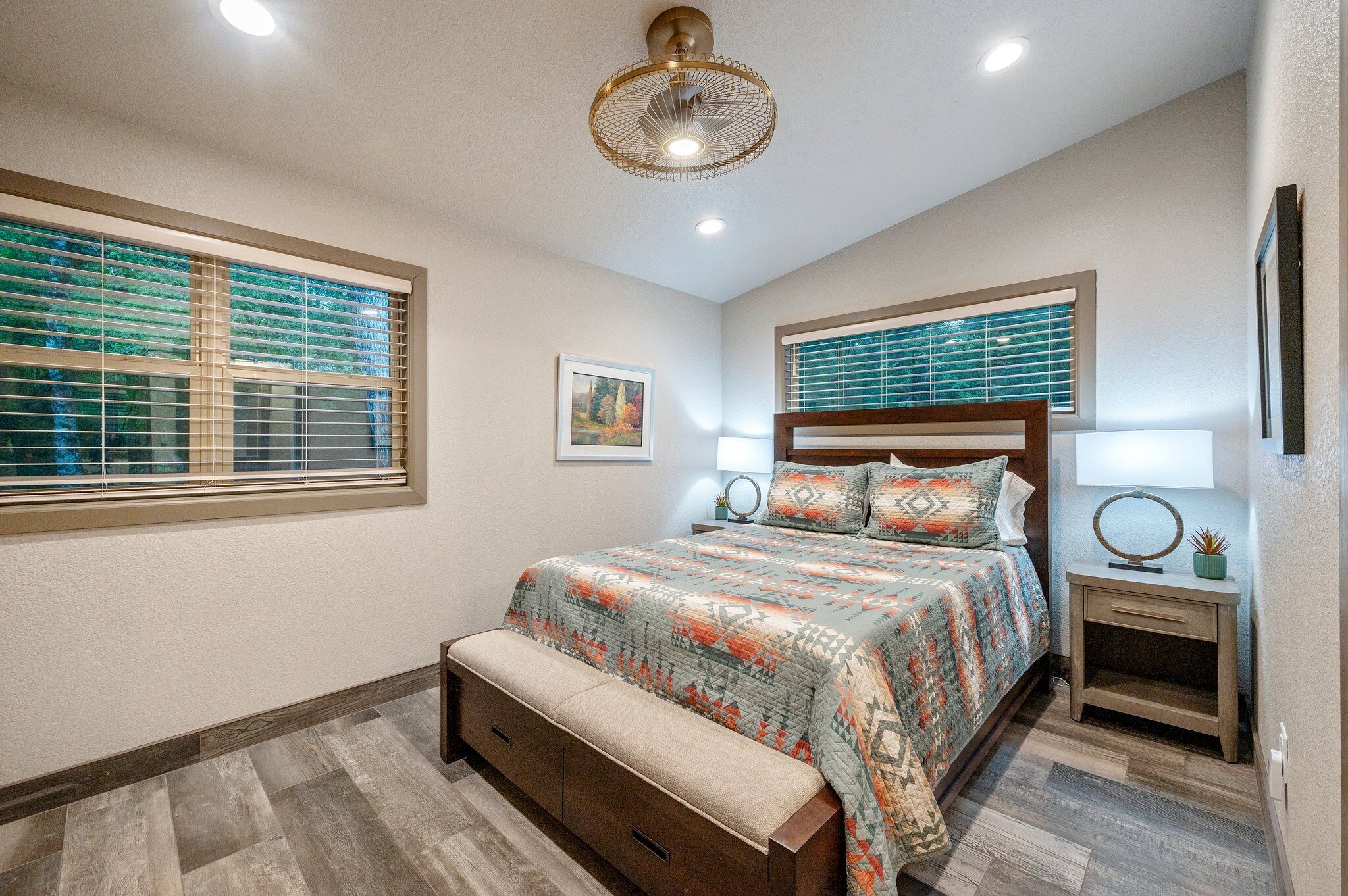 A bedroom with a bed, bench, bedside tables, and a ceiling fan.