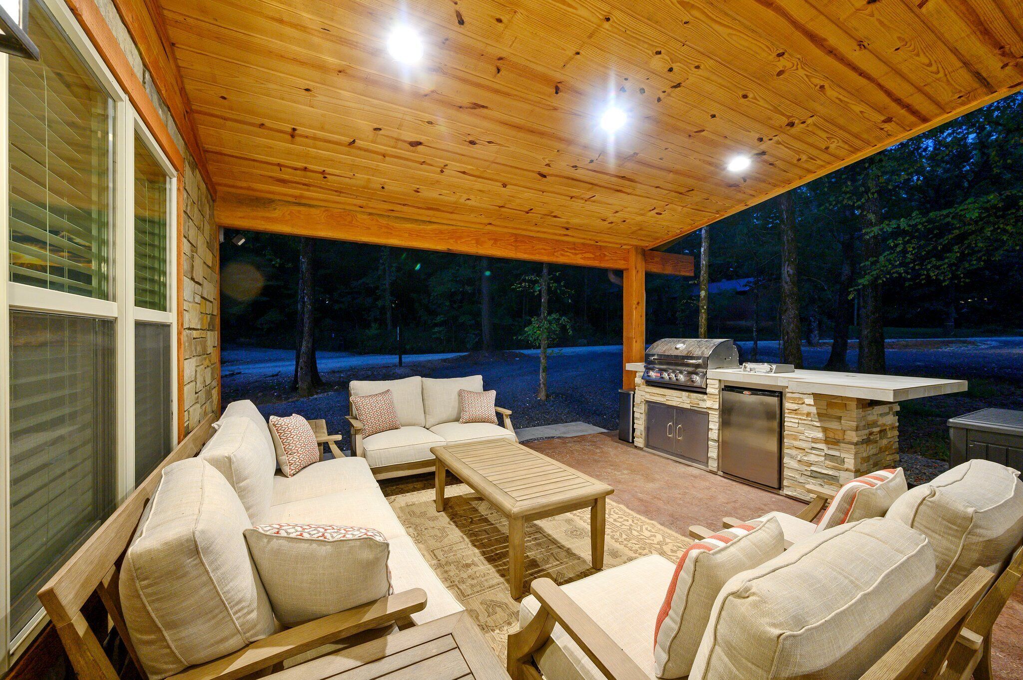An outdoor patio with a wooden ceiling, stone fireplace, and seating area.