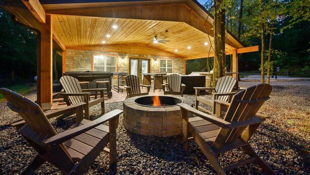 Un espace extérieur aménagé avec des sièges, protégé du soleil, comprenant des fauteuils Adirondack, un foyer et une cheminée en pierre.