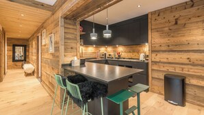 Une cuisine moderne avec des murs en bois, un îlot central, des tabourets de bar et des luminaires suspendus.