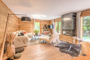 A modern living room with wooden walls, a fireplace, a sofa, a coffee table, and a TV. - Appartement Capra - Welkeys (Megève)
