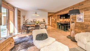 Un intérieur moderne avec un plancher en bois, un canapé blanc agrémenté d’un coussin noir, un coin repas avec des chaises et une cuisine avec des tabourets de bar.