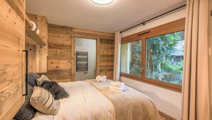 Une chambre avec des murs en bois, une grande fenêtre, un lit recouvert d’une couverture beige et une serviette posée sur le lit.