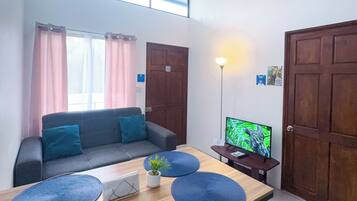 A modern living room with a sofa, a dining table with placemats, a television, and a ceiling fan.
