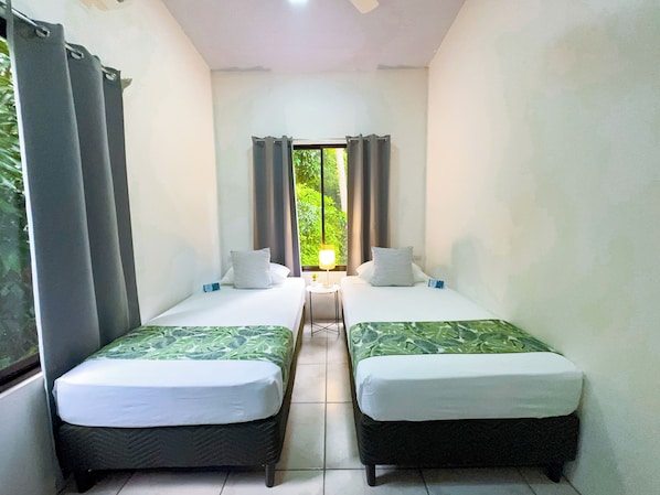 A room with two beds, a small table, and a window with curtains.