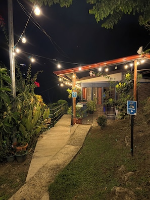 A covered outdoor area with a pathway leading to a building, surrounded by potted plants and a sign indicating a continuation path.