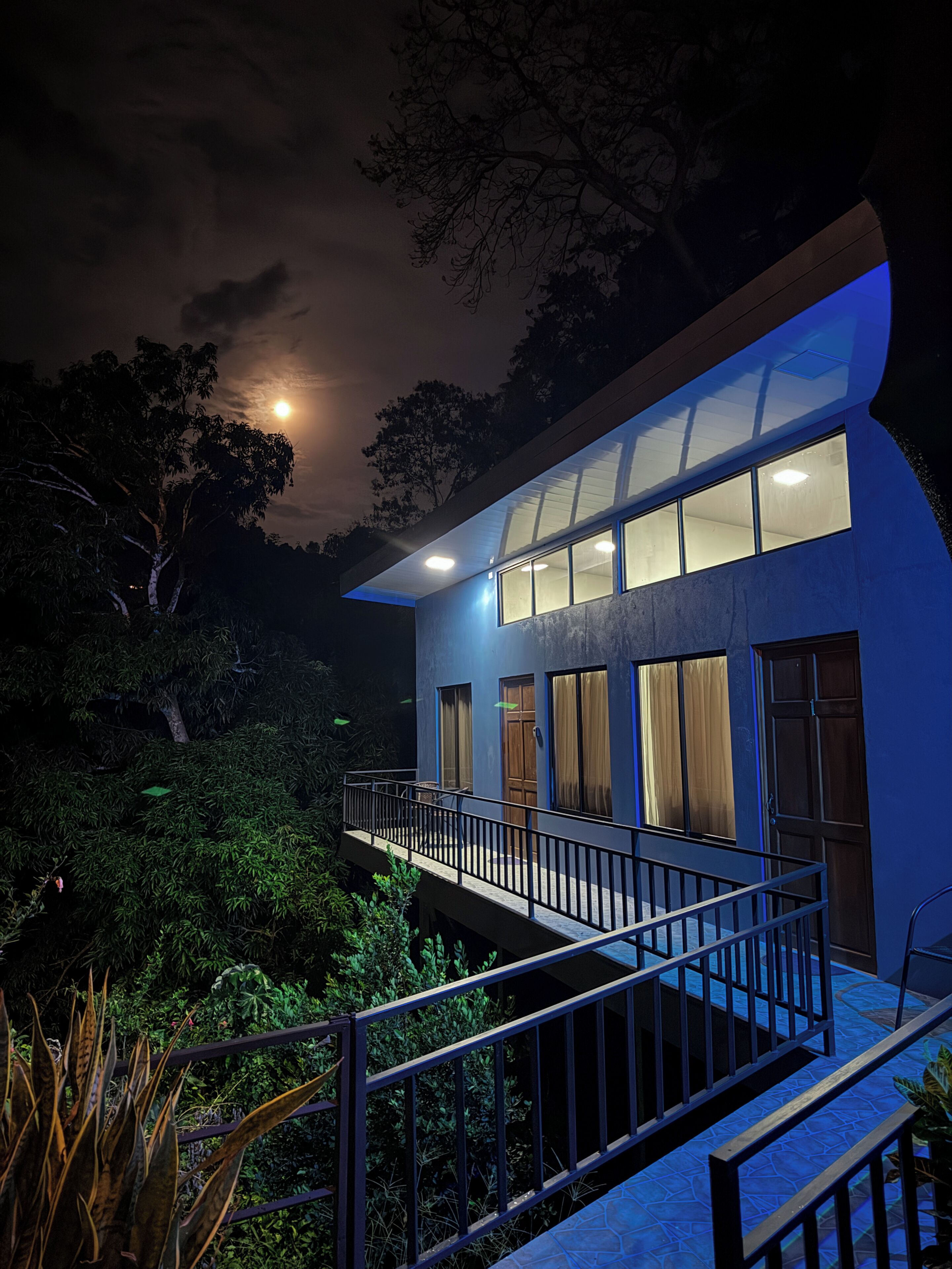 A modern house with a balcony, large windows, and a moon in the sky.
