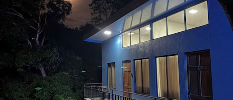 A modern house with a balcony, large windows, and a moon in the sky.