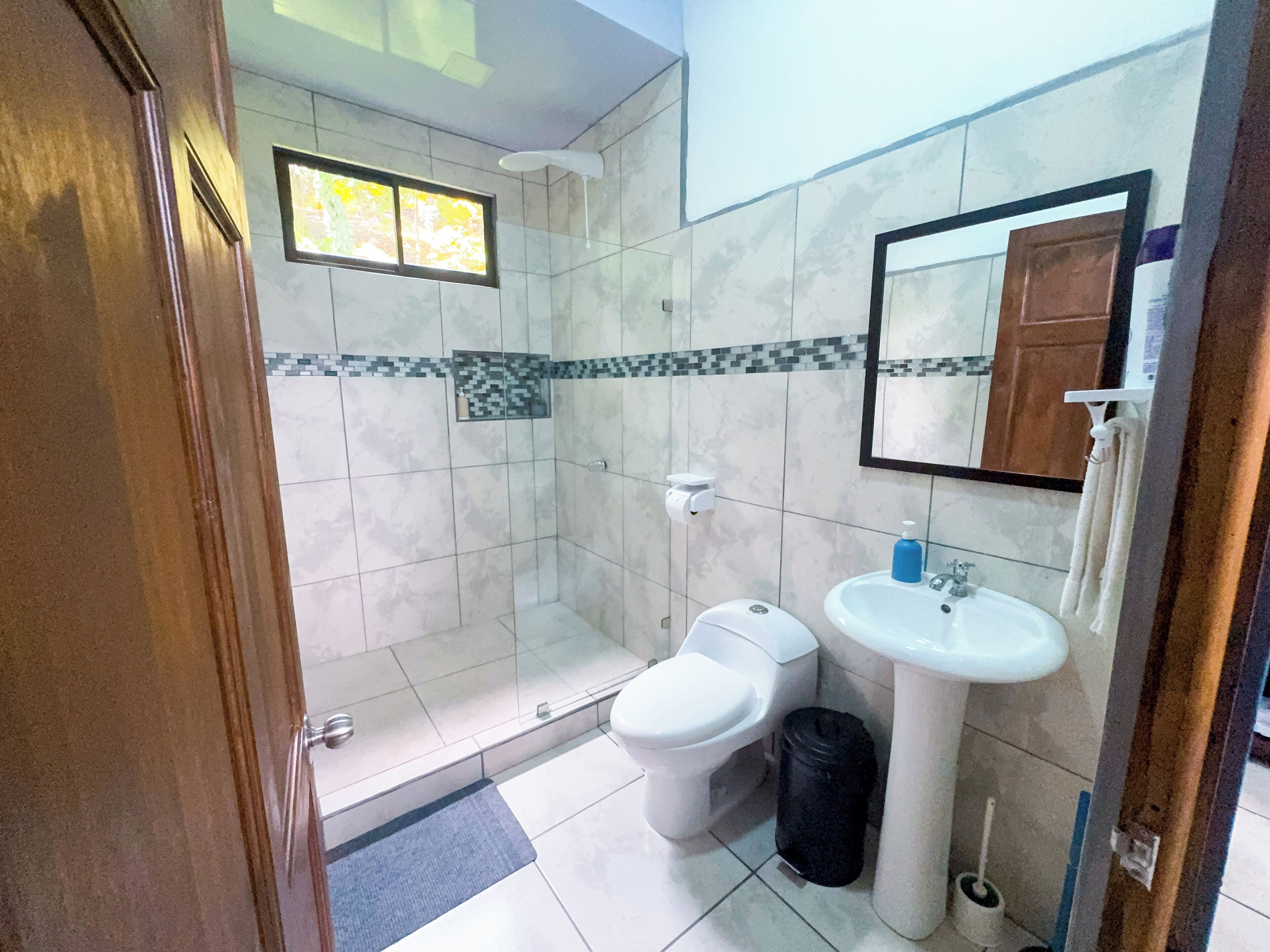 A bathroom with a shower, toilet, sink, and a mirror.