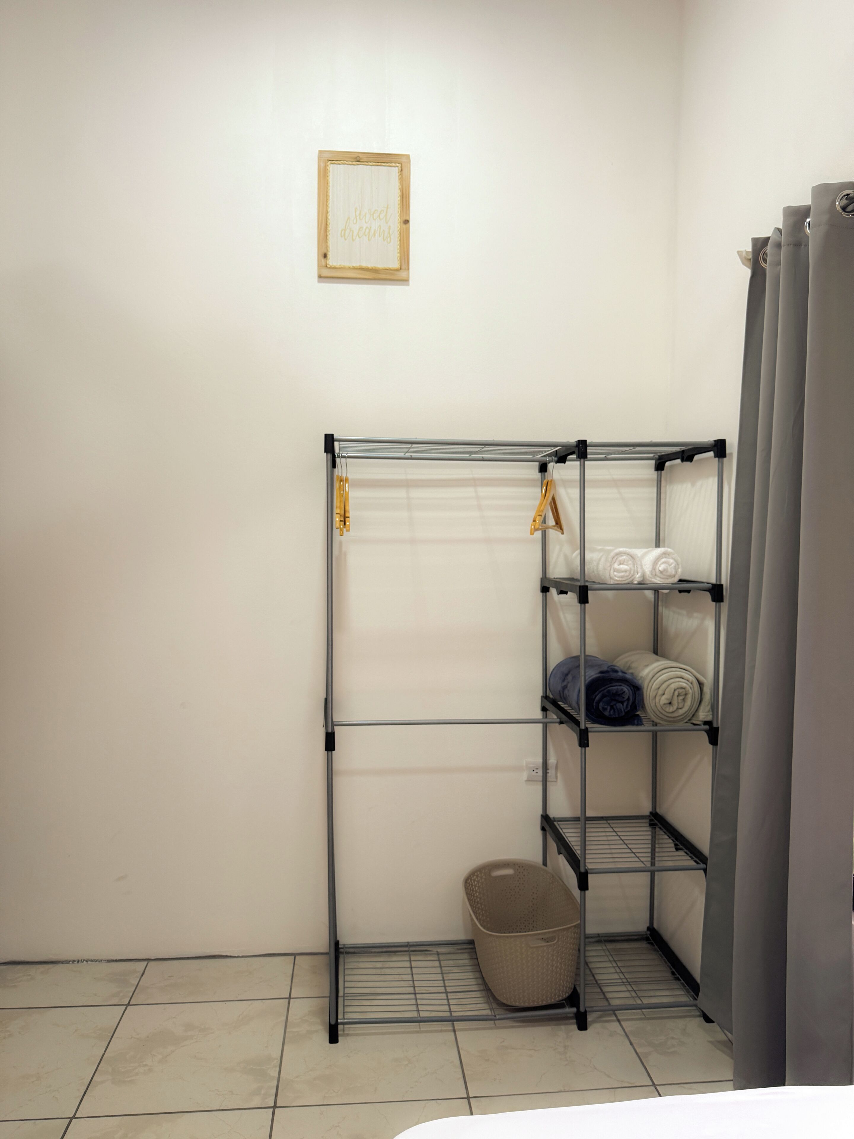Un tendedero metálico con repisas, una cesta y un cartel en una pared blanca.