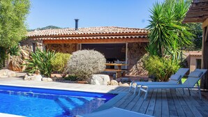 A swimming pool with lounge chairs, a stone building with a tiled roof, and surrounding greenery. - Casa Isabella Di Santa Lucia (Zonza)