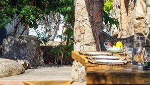 An outdoor dining area with stone pillars, a wooden table set with plates, glasses, and a bowl of fruit. - Casa Isabella Di Santa Lucia (Zonza)