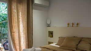A hotel room with a bed, a window with curtains, a wall-mounted air conditioner, and a small shelf with decorative items. - Casa Isabella Di Santa Lucia (Zonza)