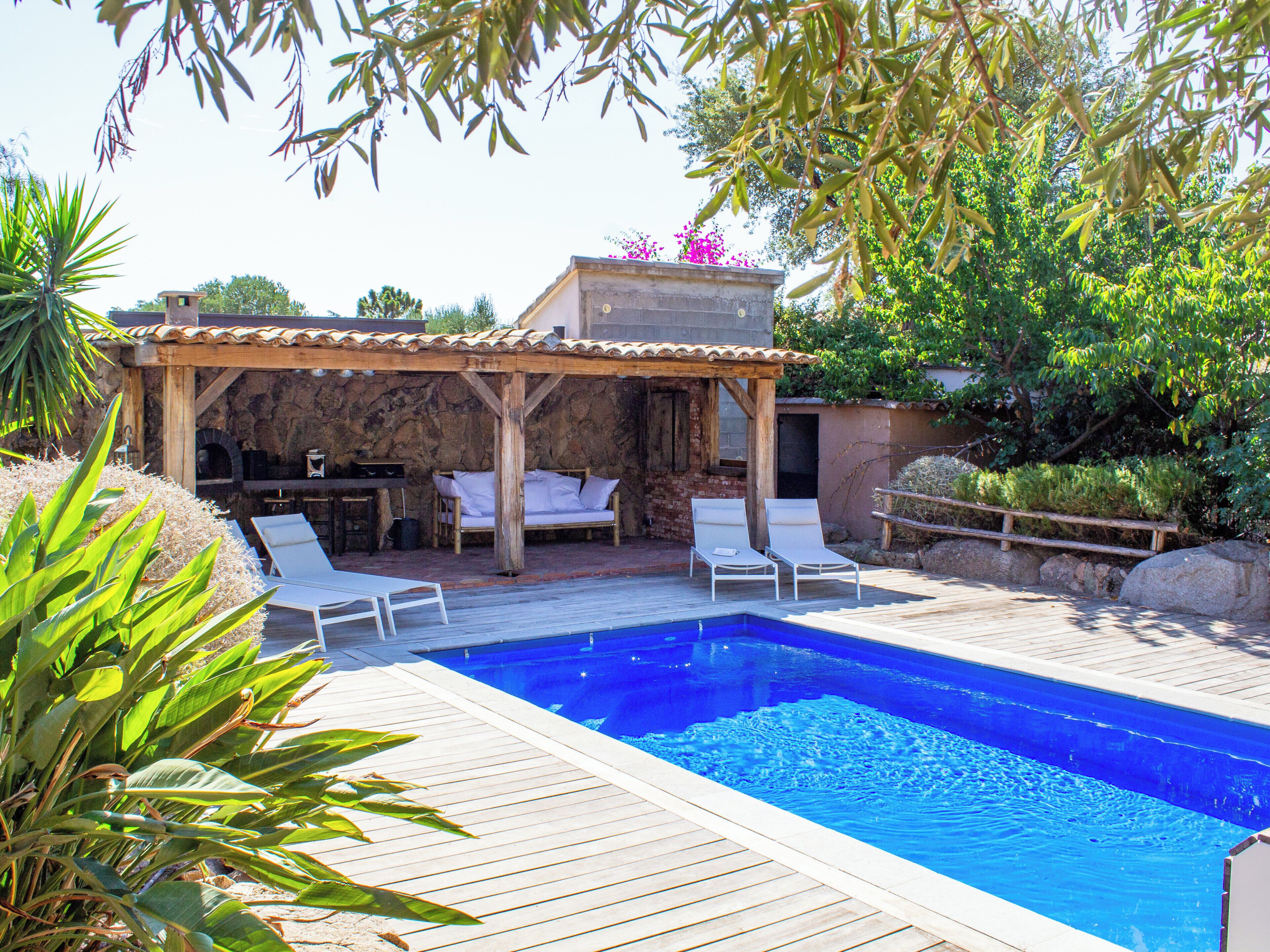 Una piscina con sillones de descanso y un pérgola de madera.
