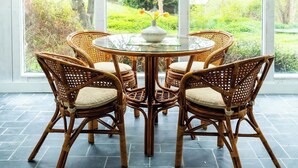 Une table ronde en verre, entourée de chaises en osier, dans une pièce dotée de grandes fenêtres.