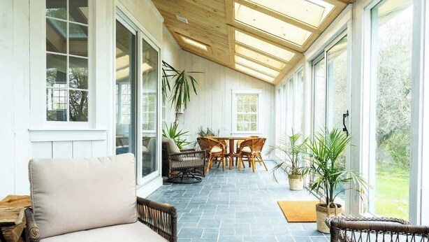 Une pièce baignée de lumière, avec un plafond en bois, de grandes fenêtres et un sol en pierre.