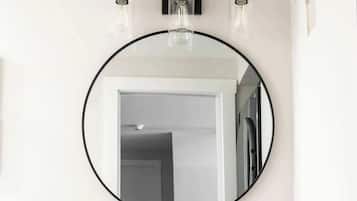 A bathroom with a round mirror, a white sink, and wooden cabinets.