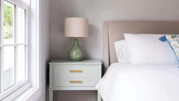 A bedroom with a bed, a nightstand with a lamp, a window, and a wooden floor.
