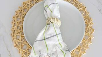 A white plate with a woven placemat, a white cloth with green stripes, and a beaded accessory on a marble surface.