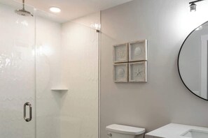 Ein Badezimmer mit Duschkabine aus Glas, Toilette, Waschbecken und einem wandmontierten Spiegel.