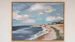 A framed painting of a beach scene with waves, sky, and distant land.