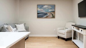 A modern living room with a painting of a beach, a sofa, a chair, and a TV mounted on the wall.