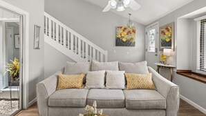 Ein Wohnzimmer mit grauem Sofa, Deckenventilator und Bildern an den Wänden.