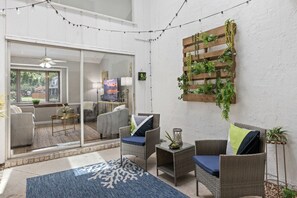 Un patio acogedor con mobiliario de mimbre, una alfombra azul y una pared vegetal de madera.