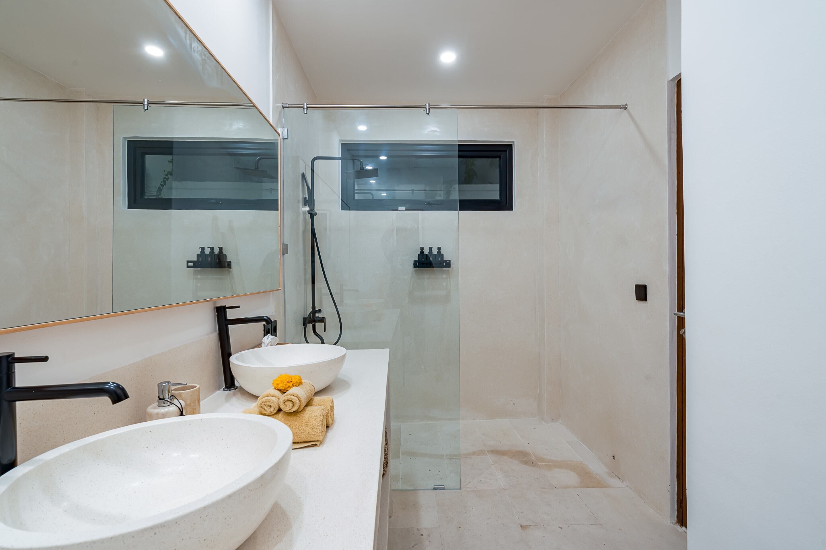A modern bathroom with a large white sink, a mirror, and a glass-enclosed shower.