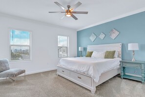 A bedroom with a bed, two bedside tables with lamps, a ceiling fan, and two windows with blinds. - Luxury 4-BR Oasis with Private Pool, Game Room & Beach Access! (Melbourne Beach)